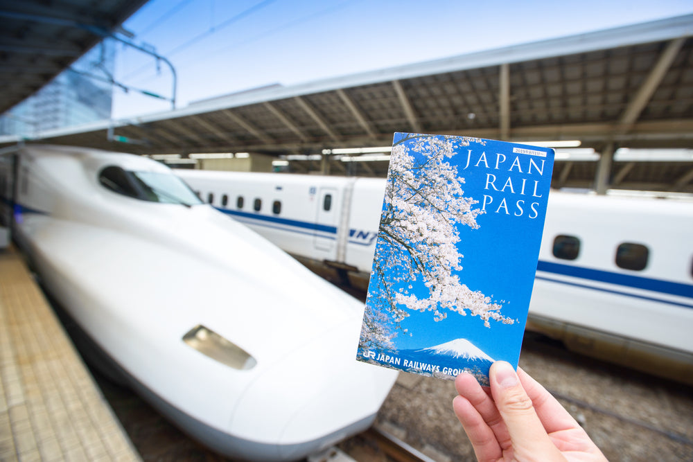Japan Rail Pass Image, hand hold JR Pass ticket in front of Shinkansen at Tokyo Station.